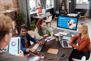 Marketing team working at a shared desk with laptops and notes, beside a monitor displaying an agency presentation, representing Meta Ads budget planning for South African businesses