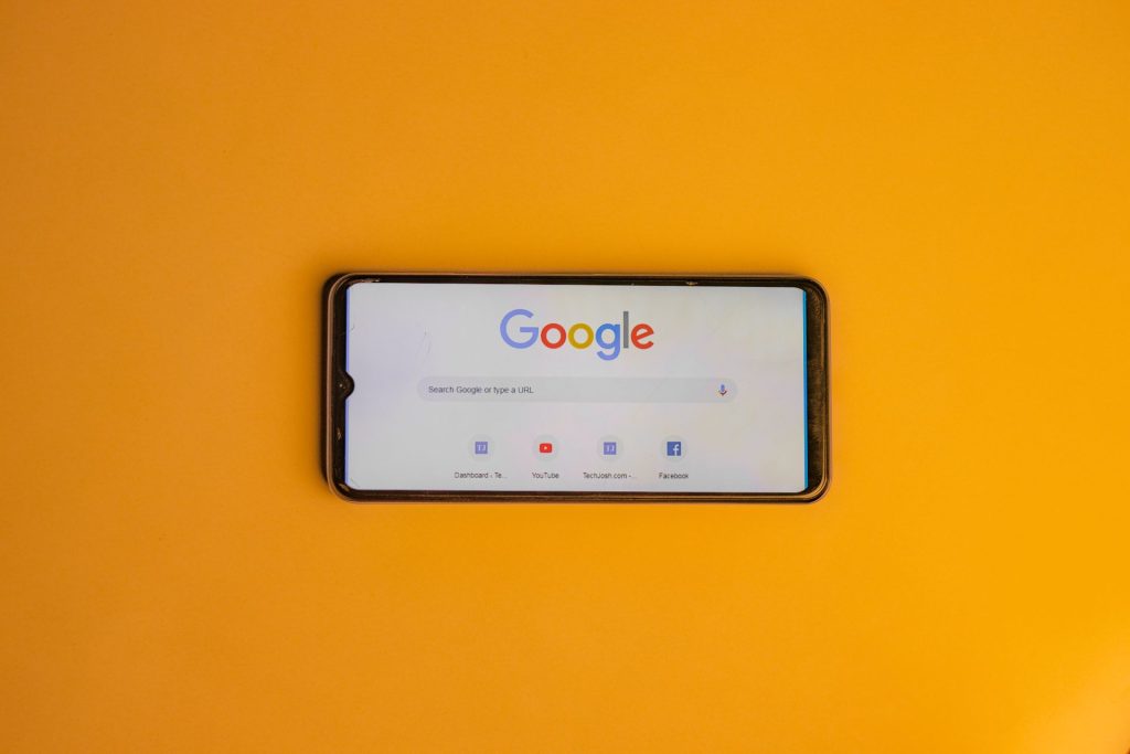 Smartphone showing the Google search homepage on an orange background.